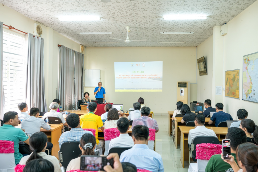 A seminar in a classroom with attendees seated at desks, a speaker at the front, and a presentation on a projector screen.