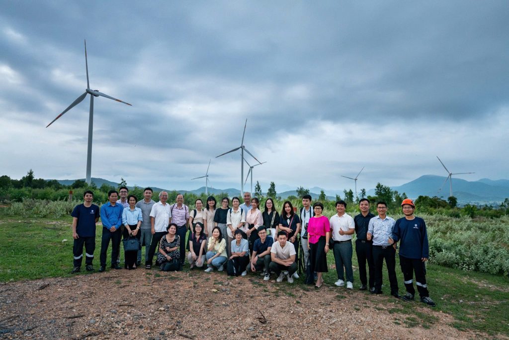 A group of people poses in front of wind turbines on a cloudy day.